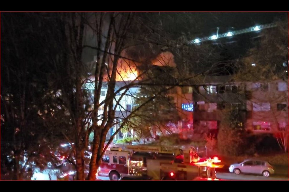 photo of a low apartment building at night, on fire. red lights of the fire engines. 